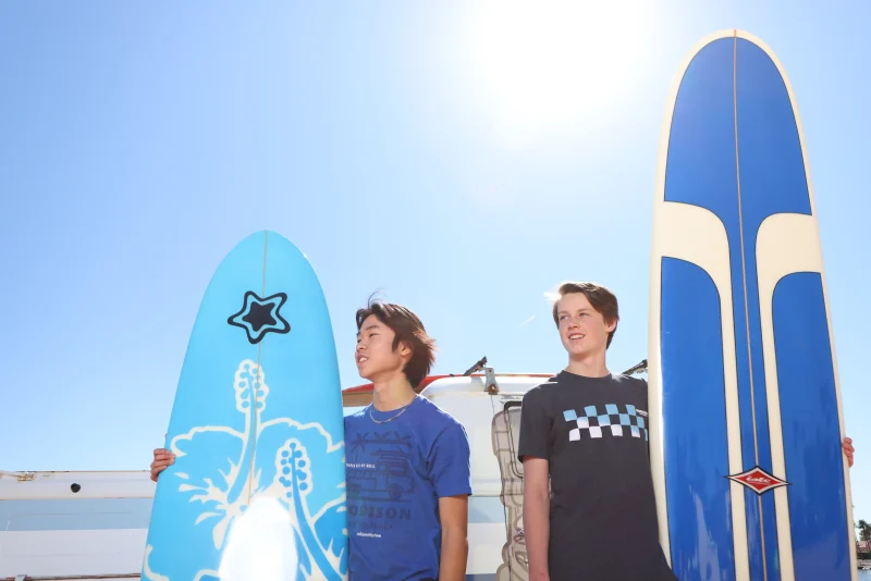2 male teenagers standing with a surfboard on each side